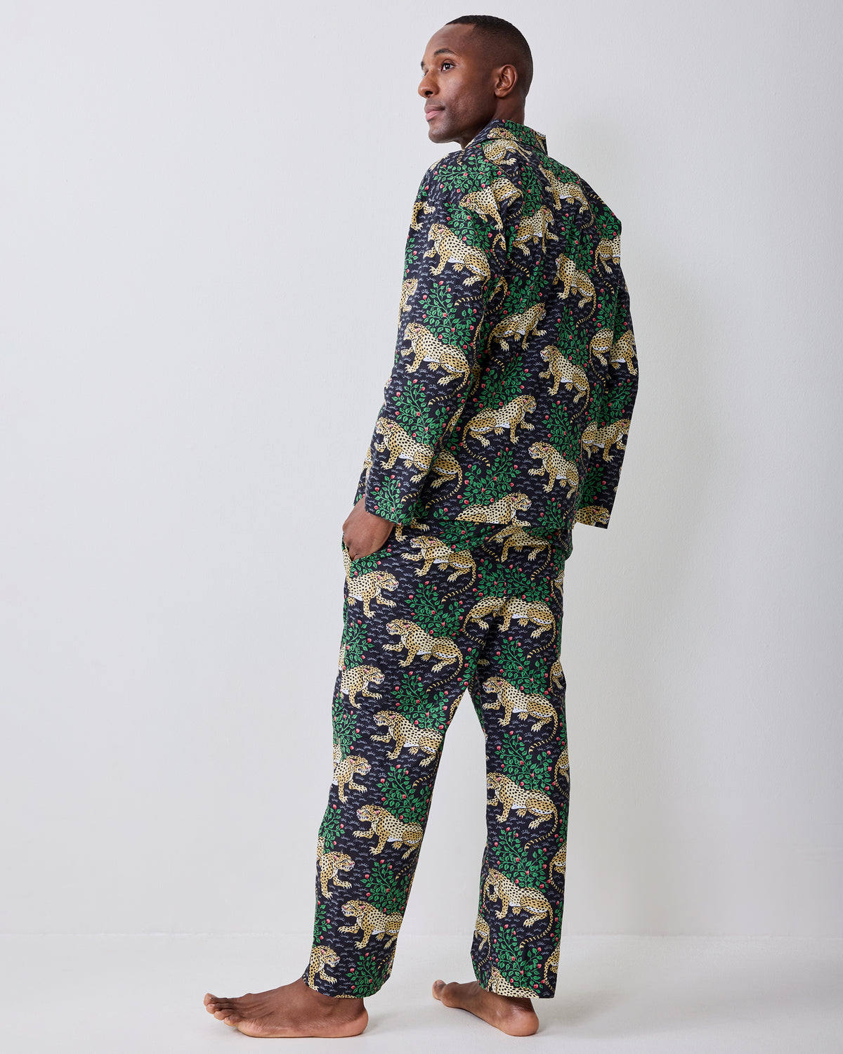 Rear three-quarter view of a person wearing a dark patterned button-front shirt and matching trousers with yellow spotted cats and green foliage.