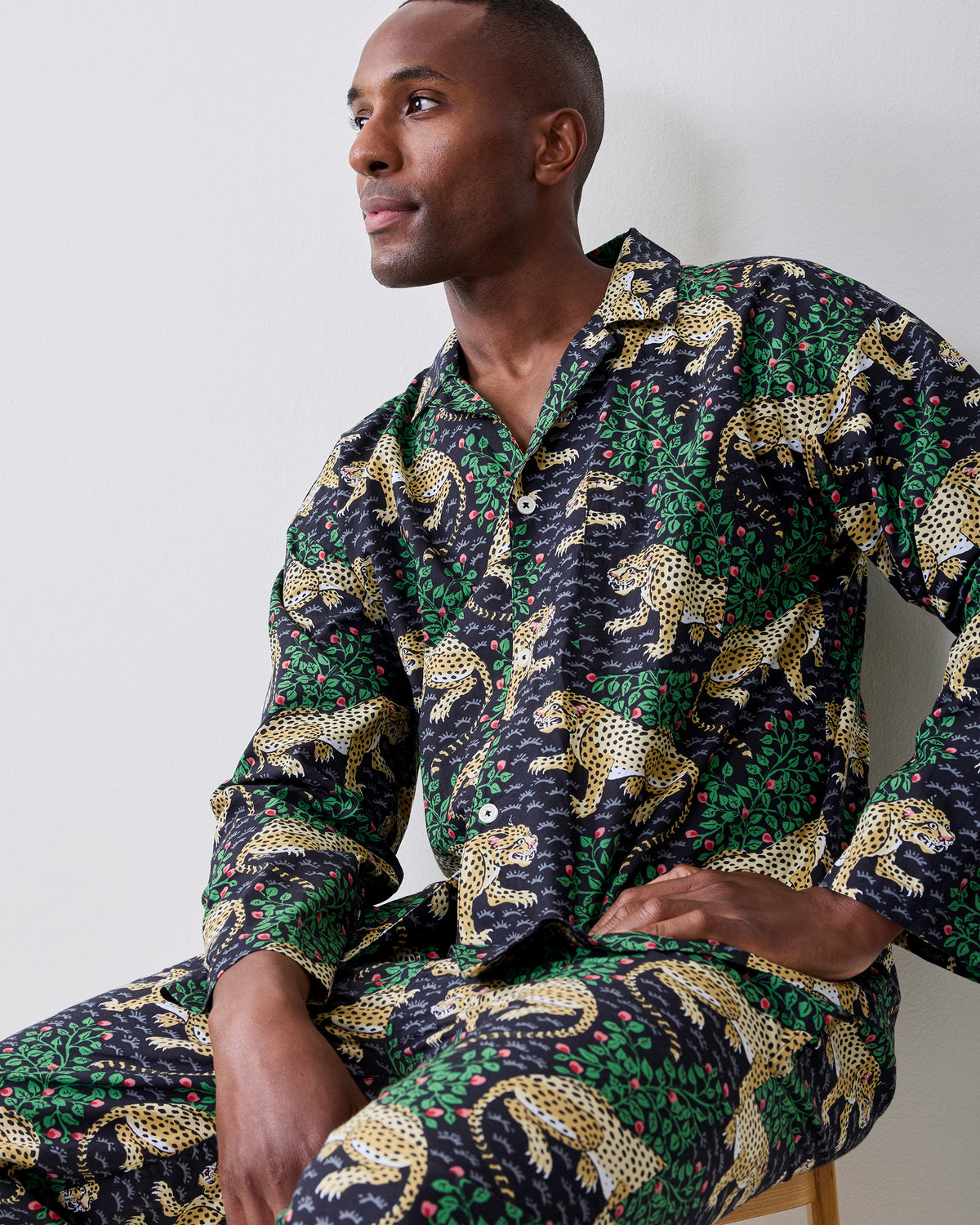 Person seated wearing a dark patterned button-front shirt and matching trousers with yellow spotted cats and green foliage.