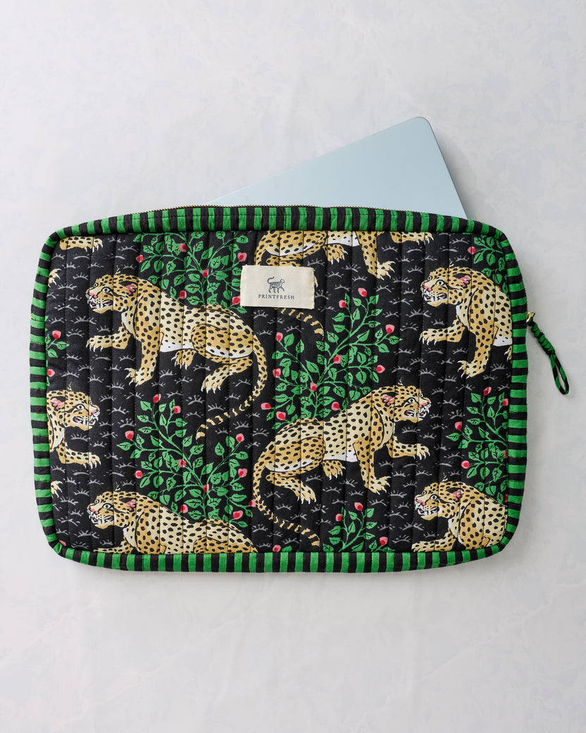 Black quilted laptop sleeve with green trim, leopard and leafy floral print, zipper, and Printfresh label, shown with a laptop partially inserted.