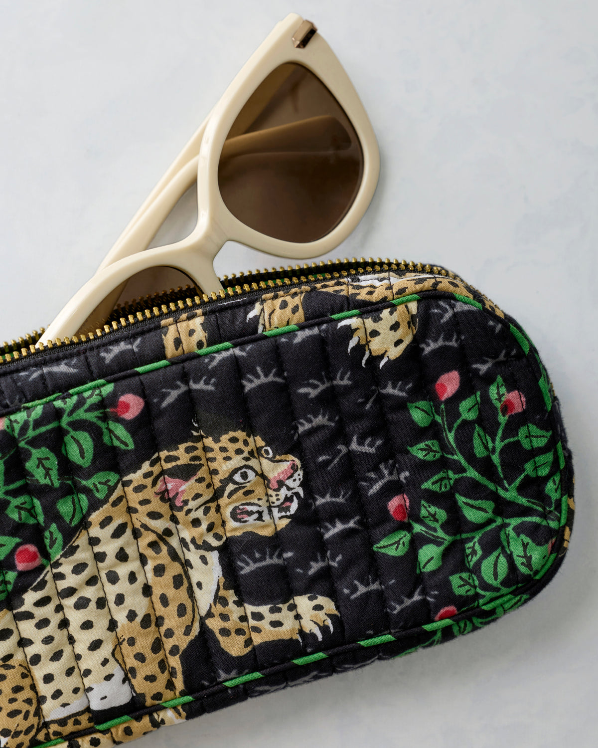 Close-up of the Bagheera Ink quilted sunglasses case with white sunglasses partly visible behind it.