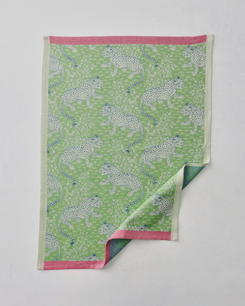 Green Bagheera jacquard tea towel with a repeating spotted big-cat pattern and pink edging, shown with one corner folded back.