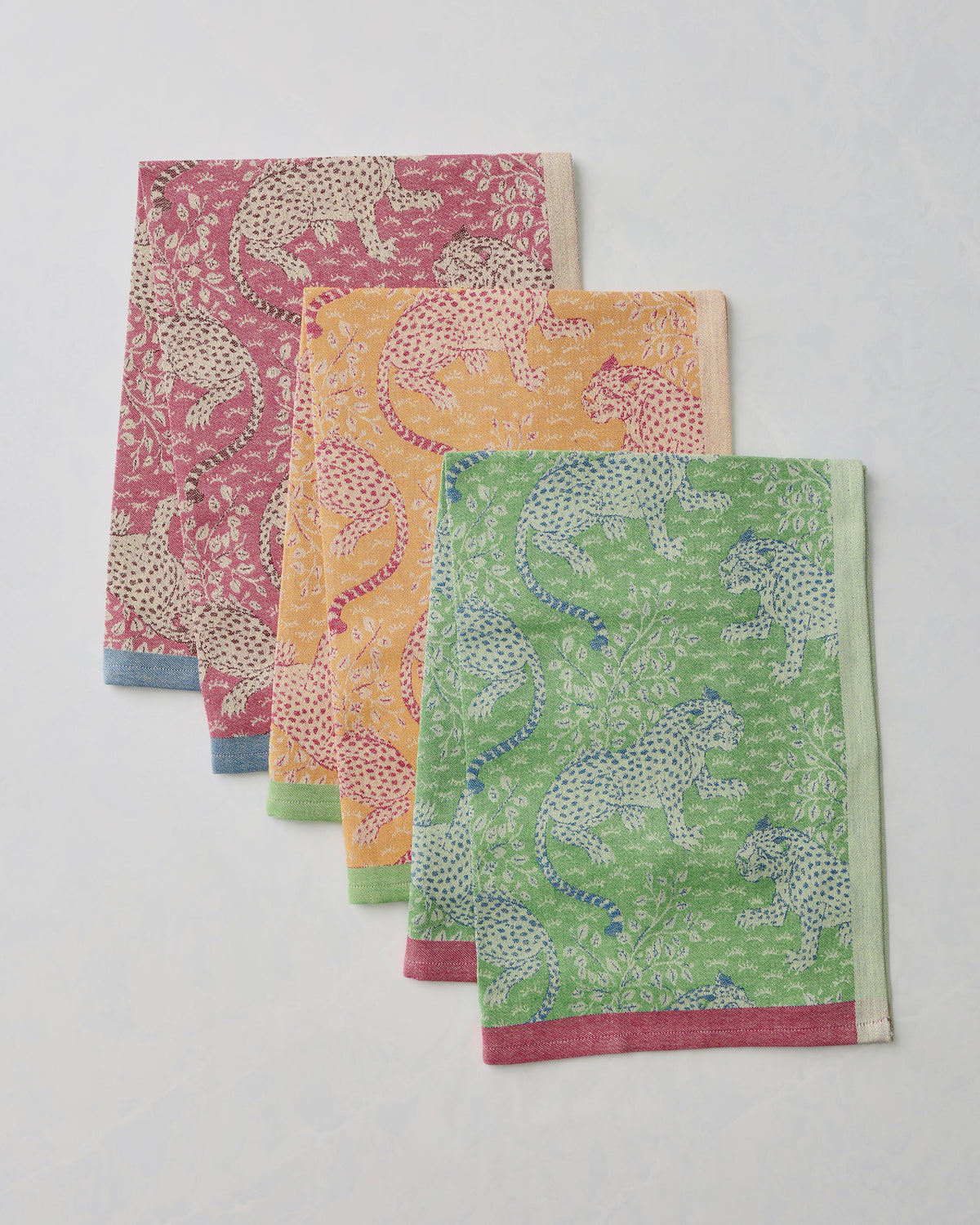 Three Bagheera jacquard tea towels in hot pink, yellow, and green, layered to show their leopard-and-floral patterns and contrasting borders.