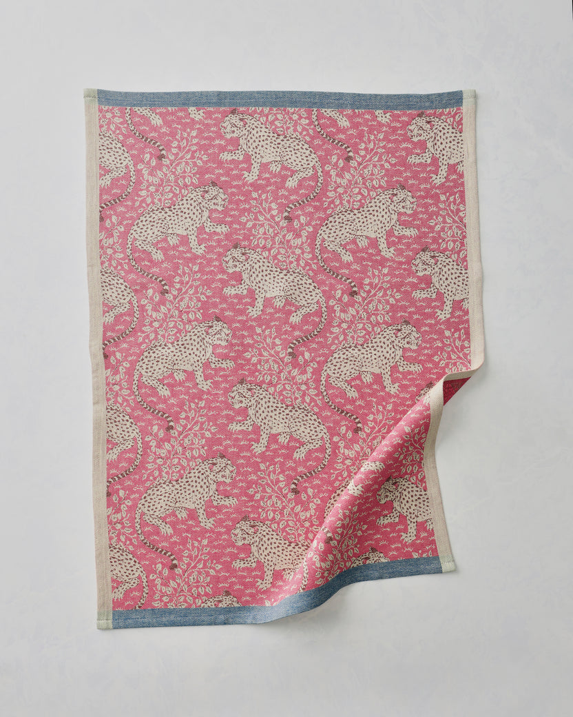 Hot pink Bagheera jacquard tea towel with a repeating leopard-and-floral pattern, shown flat with one corner folded back.