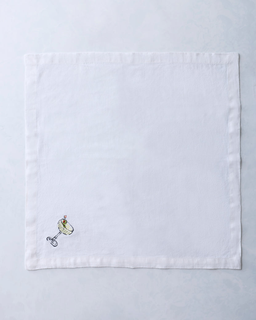 White square dinner napkin embroidered with a small cocktail glass and garnish motif near one corner.