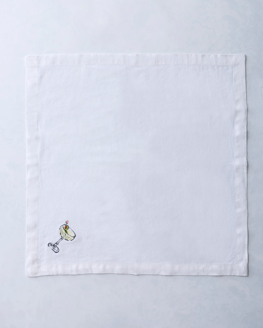 White square dinner napkin embroidered with a small cocktail glass and garnish motif near one corner.