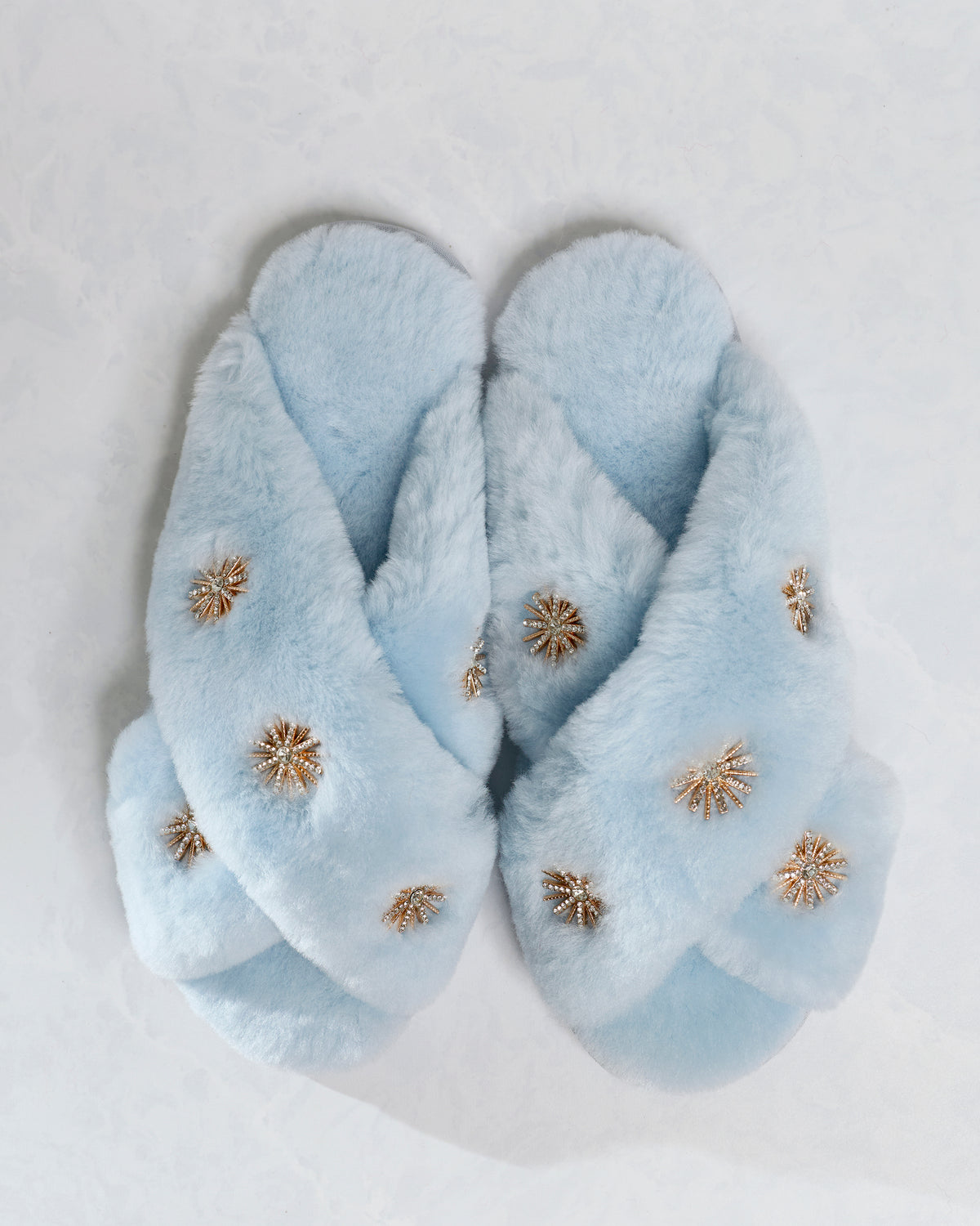 Dusty blue sheepskin slippers with rhinestone embellishments, shown as a pair from above.