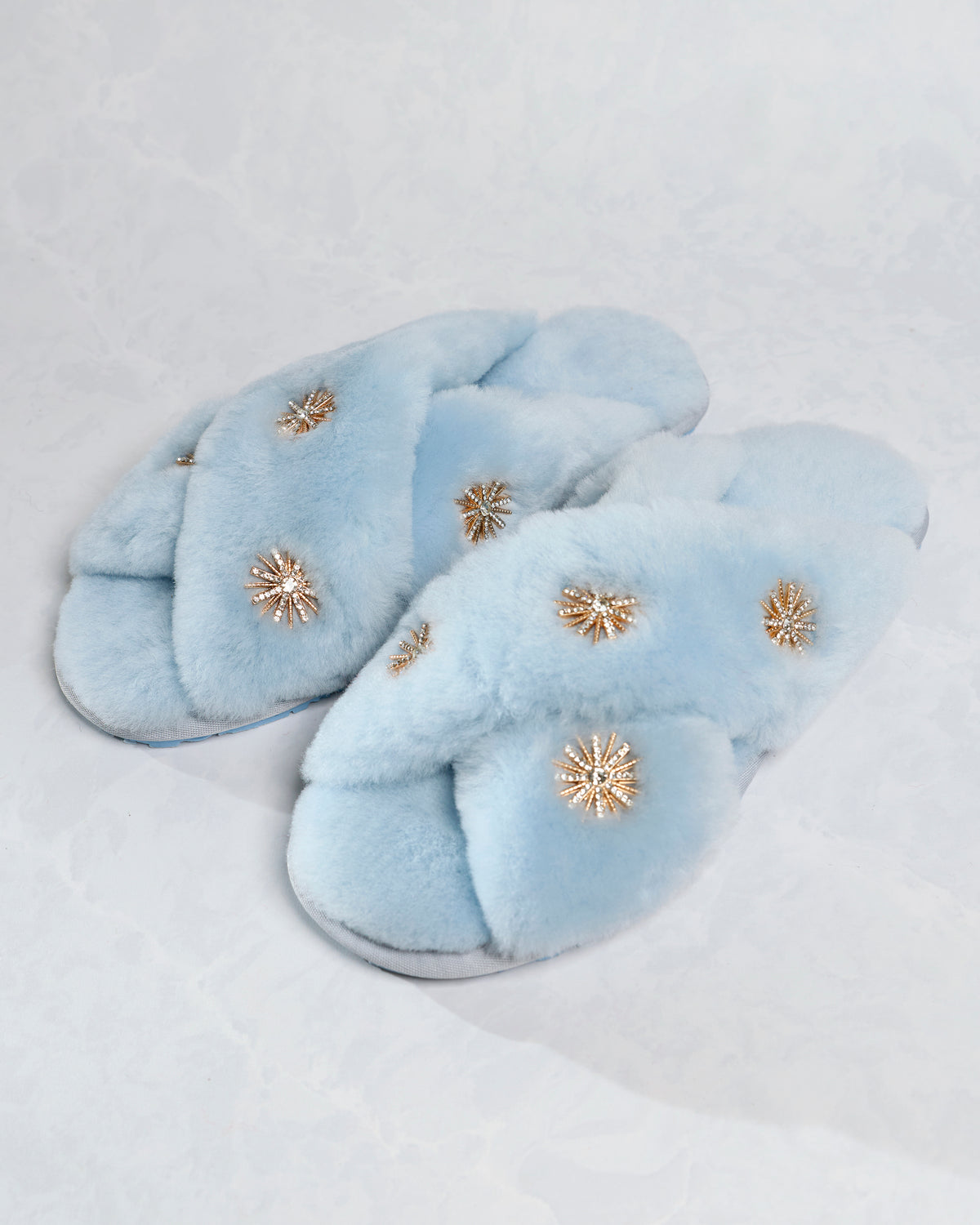 Dusty blue sheepskin slippers with rhinestone embellishments, shown from a low side angle.