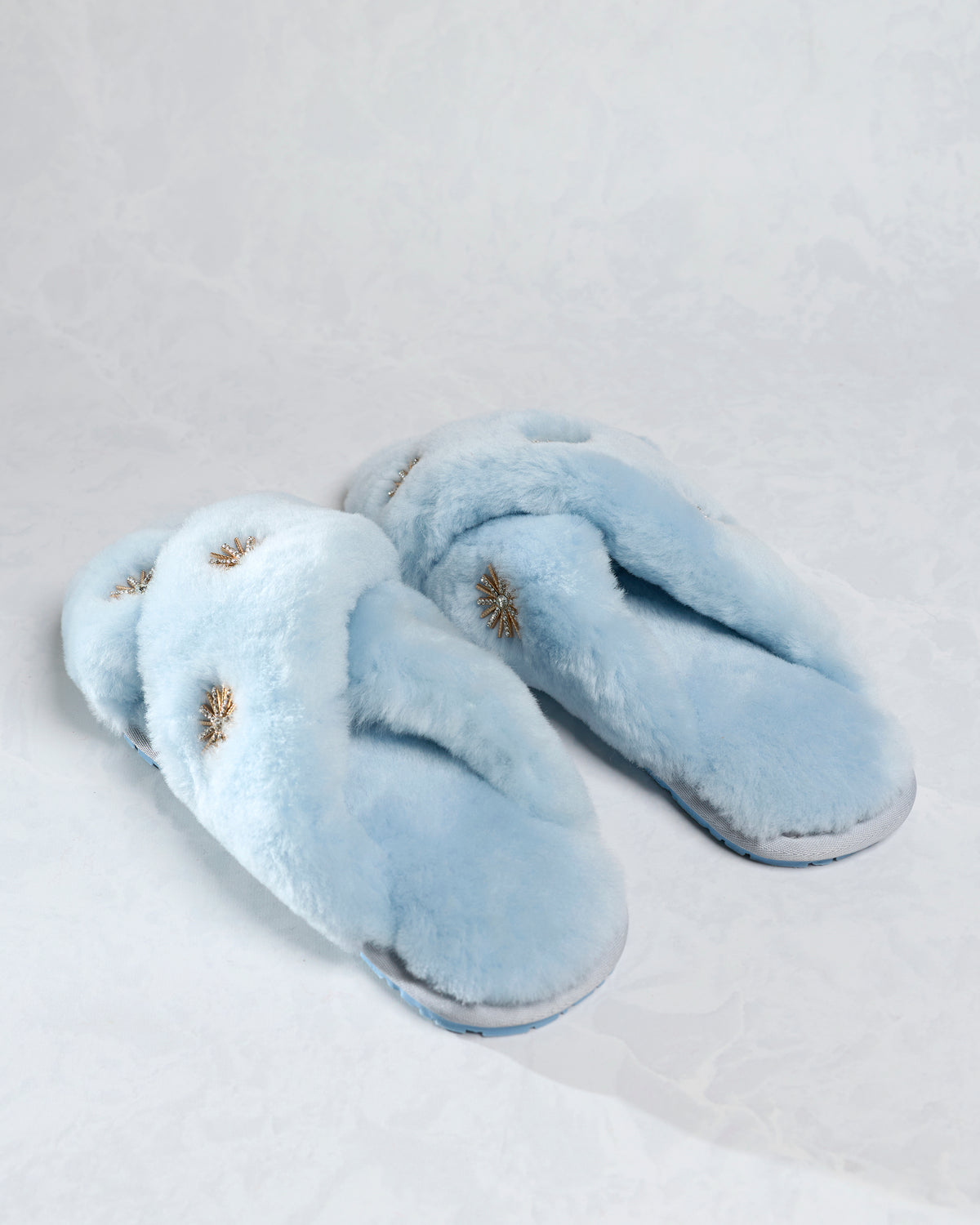 Dusty blue sheepskin slippers with rhinestone embellishments, shown together from a side angle.