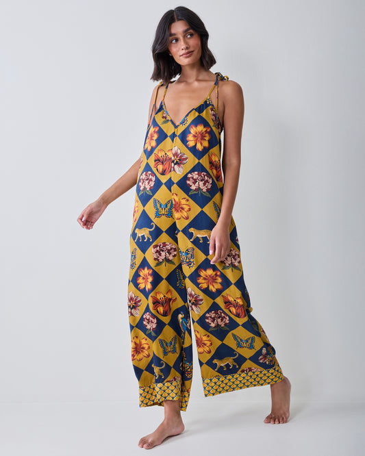 Front view of the Botanical Checkerboard Jaipur jumpsuit with tie shoulder straps, a V-neckline, wide legs, and floral, butterfly, and leopard motifs.