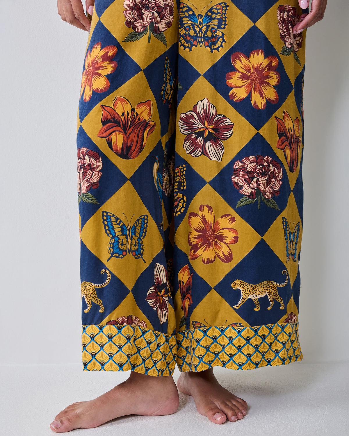Close-up of the Botanical Checkerboard Jaipur jumpsuit pants showing the wide legs, patterned hems, and floral, butterfly, and leopard motifs.