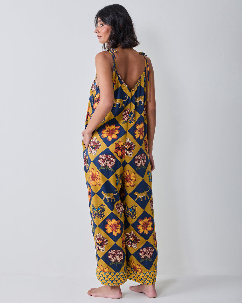Back view of the Botanical Checkerboard Jaipur jumpsuit with tie shoulder straps, a V-shaped back neckline, wide legs, and floral, butterfly, and leopard motifs.
