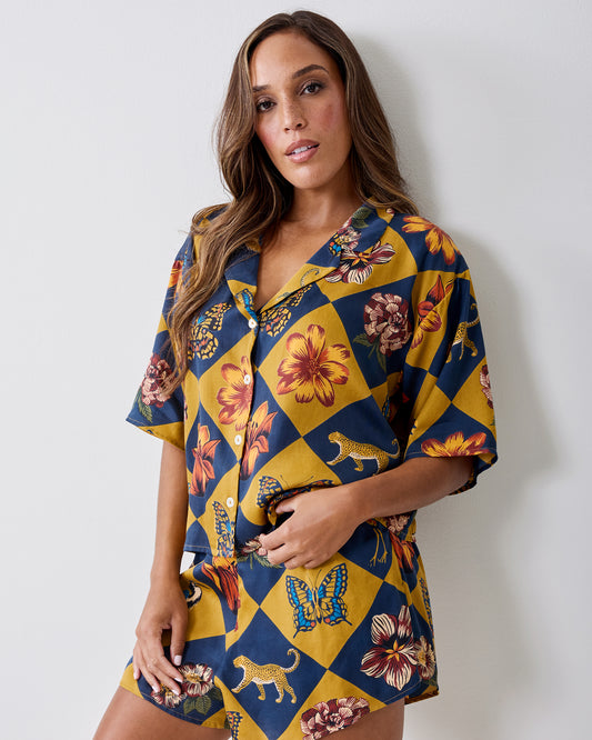 Front view of the Botanical Checkerboard Sweet Dreams pajama set with a short-sleeve button-front top and matching shorts featuring floral, butterfly, and leopard motifs.