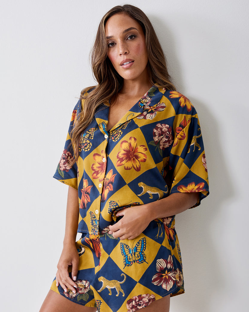 Front view of the Botanical Checkerboard Sweet Dreams pajama set with a short-sleeve button-front top and matching shorts featuring floral, butterfly, and leopard motifs.