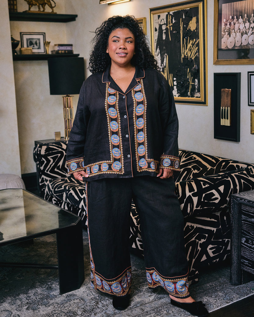 Person wearing the black Addison pajama shirt and pants with blue-and-orange circular trim, standing in a living room.
