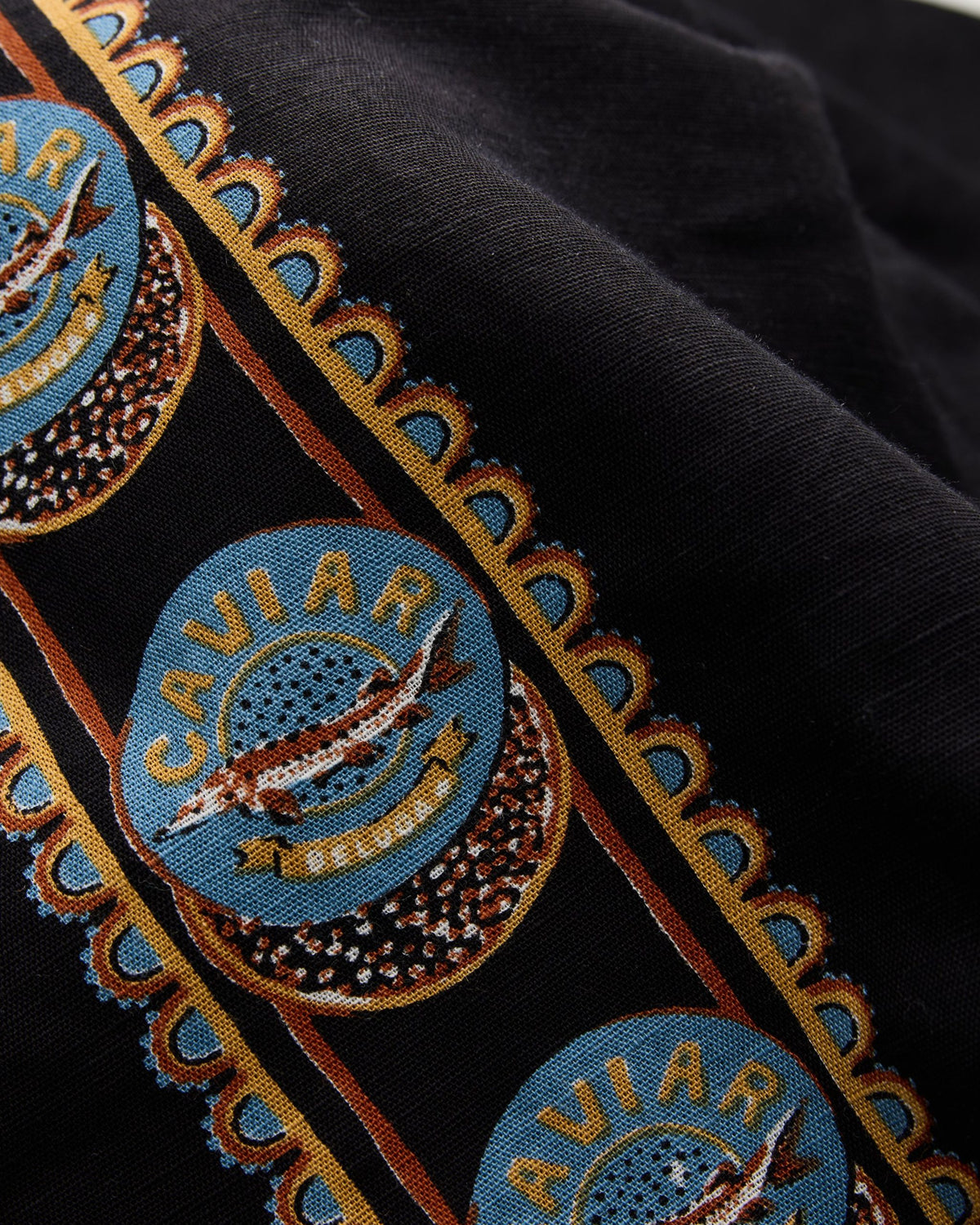 Close-up swatch of the Addison set pattern with black fabric, blue circular emblems, and gold lettering.