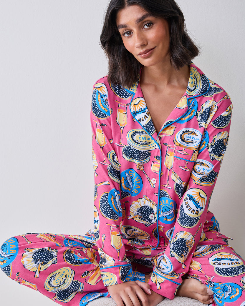 Model seated wearing the hot pink Champagne & Caviar long pajama set with a button-front top and matching pants.