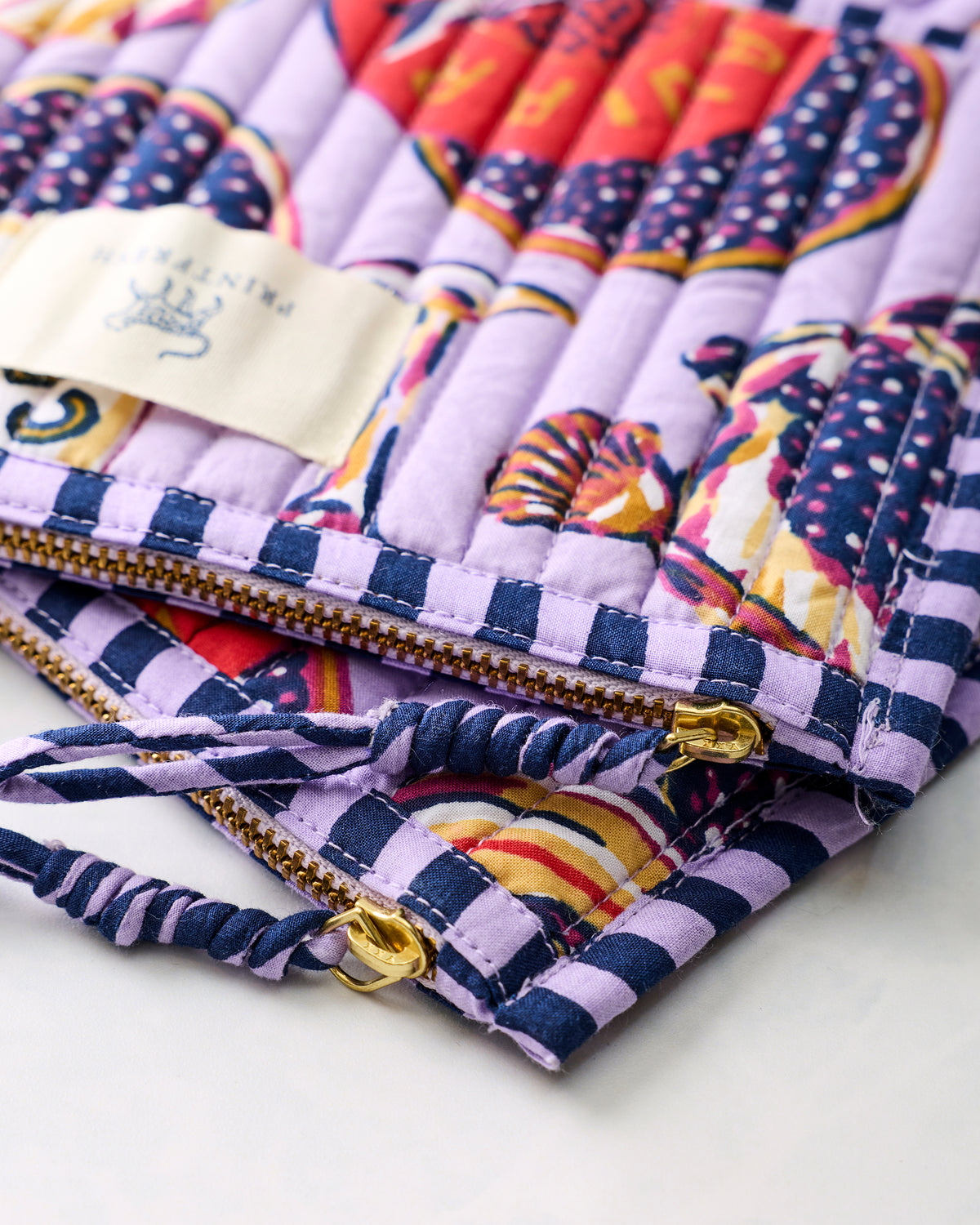 Close-up of the lavender Champagne and Caviar pouch duo showing gold-toned zippers, pulls, and twisted fabric wrist loops.