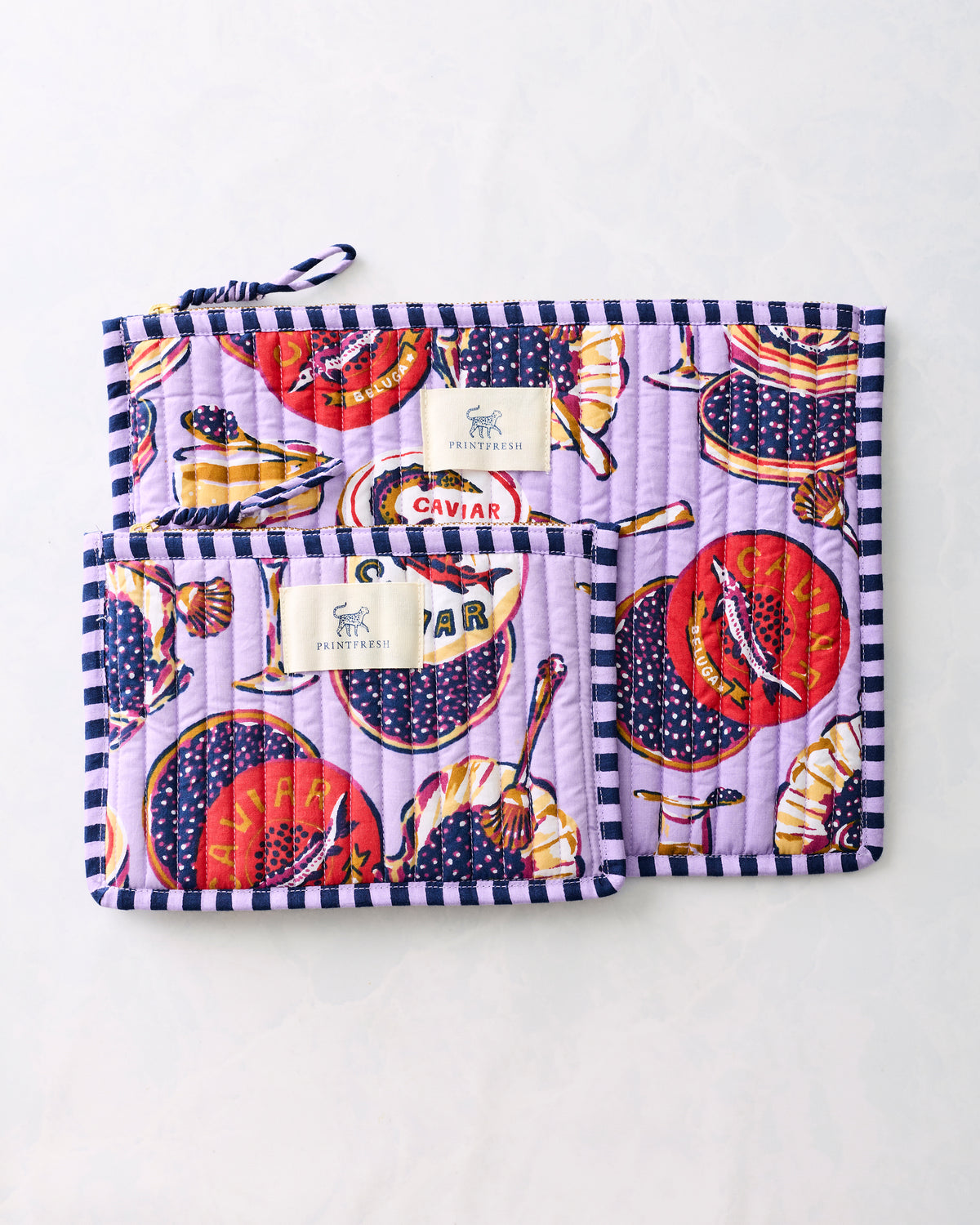 Two lavender Champagne & Caviar flat pouches with striped trim, overlapping to show both sizes.