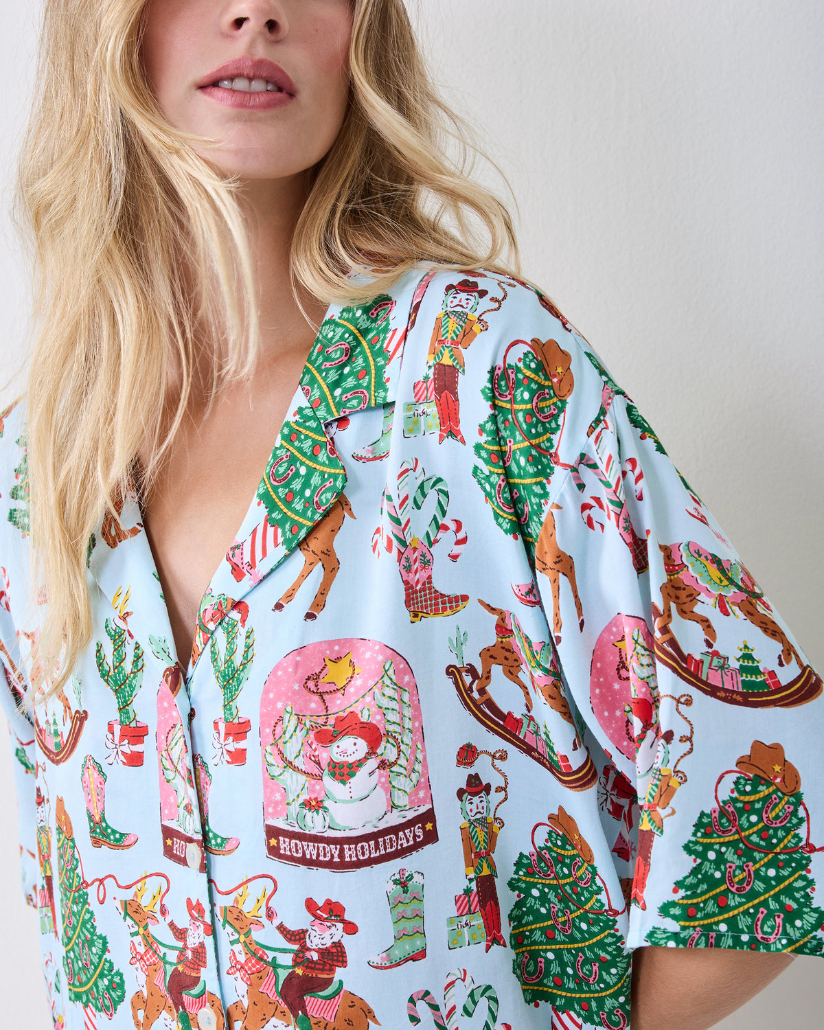 Close-up of the short-sleeve button-down top in the Cowboy Christmas print, showing reindeer, Christmas trees, boots, and snow globes.