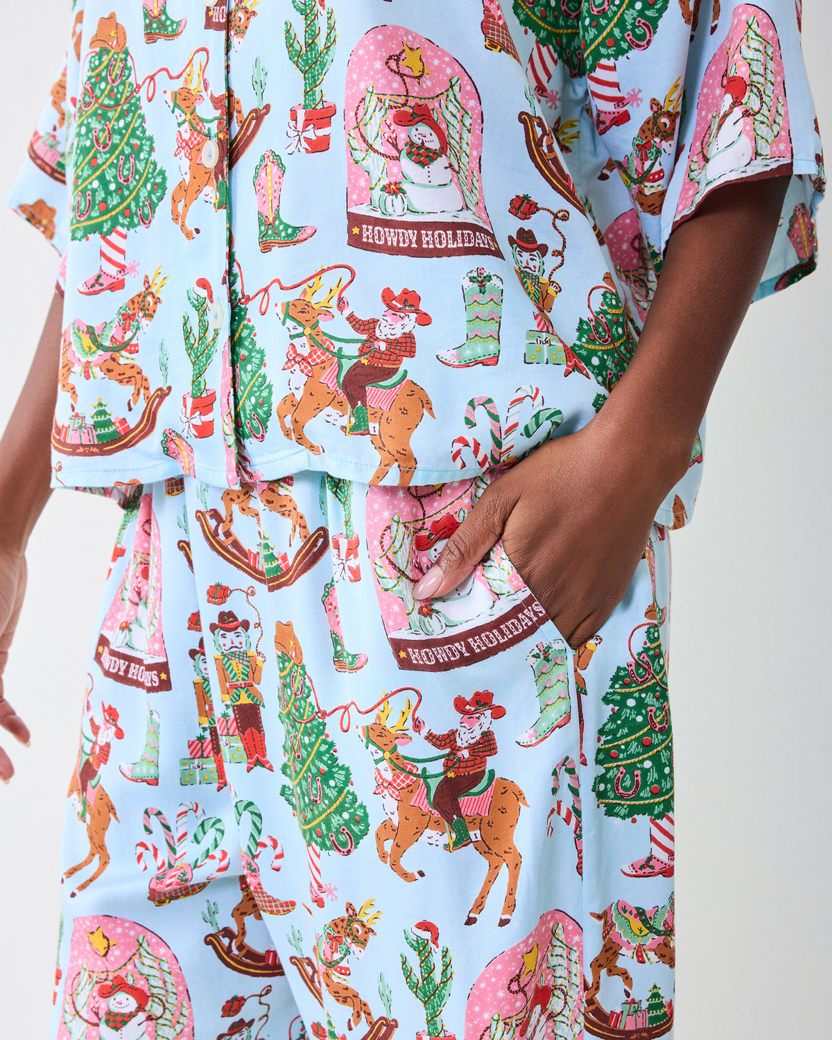 Close-up of the pale blue Cowboy Christmas pajama top and pants, showing the printed holiday Western motifs and a hand in the pants pocket.
