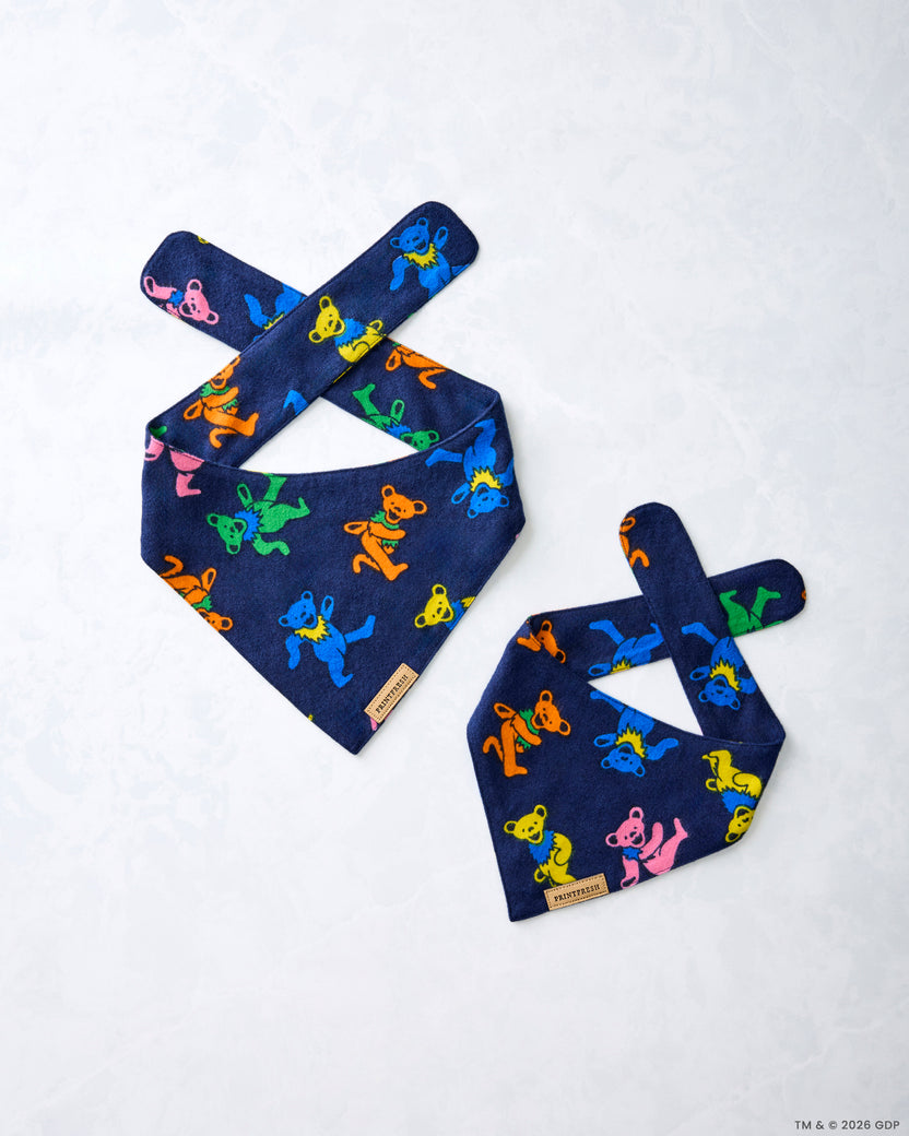 Two navy Dancing Bears pet bandanas laid flat, showing crossed tie straps and colorful bear figures.