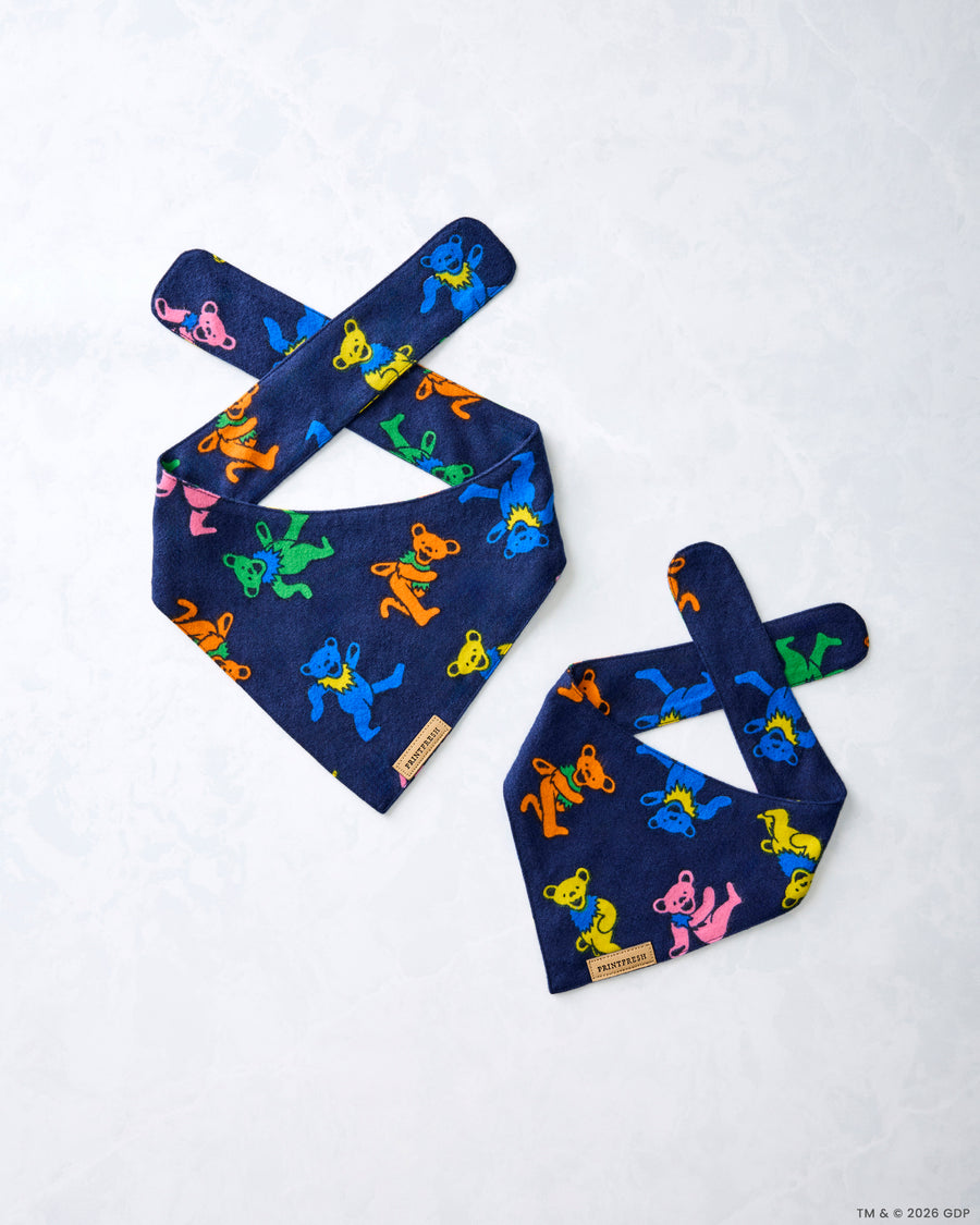 Two navy Dancing Bears pet bandanas laid flat, showing crossed tie straps and colorful bear figures.