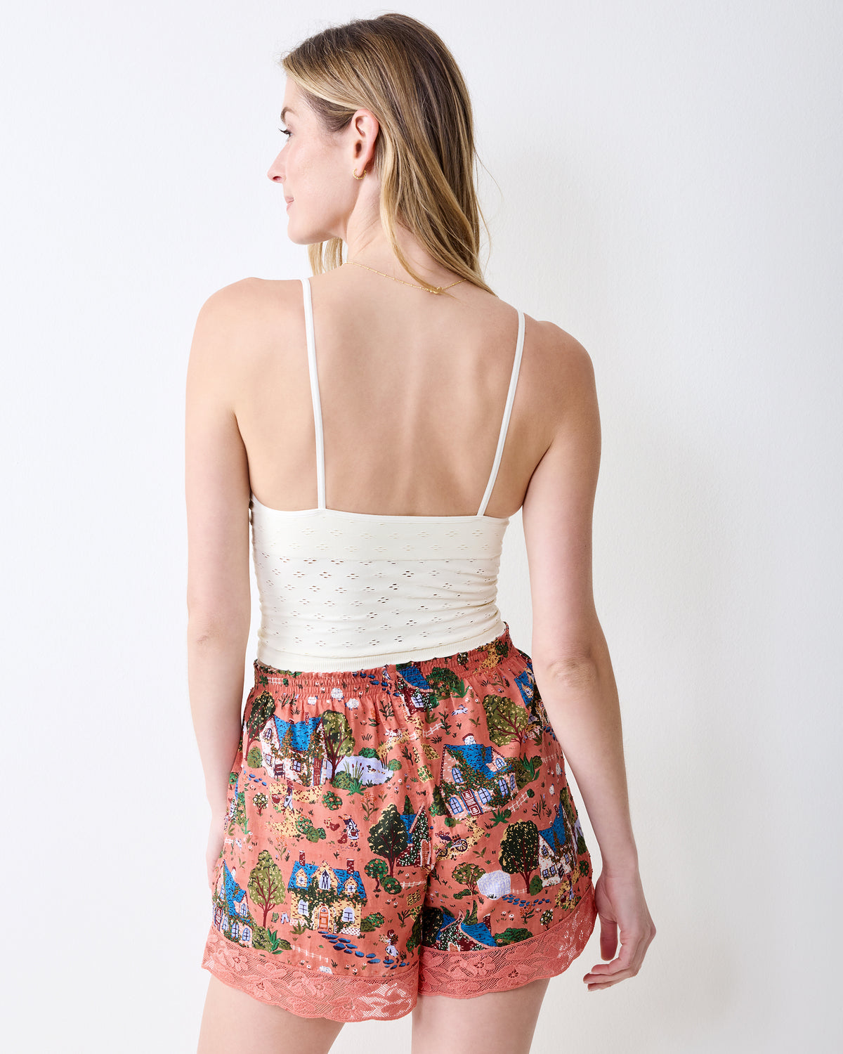 Back view of dusty rose pajama shorts with a cottage-and-tree print and lace-trim hems.