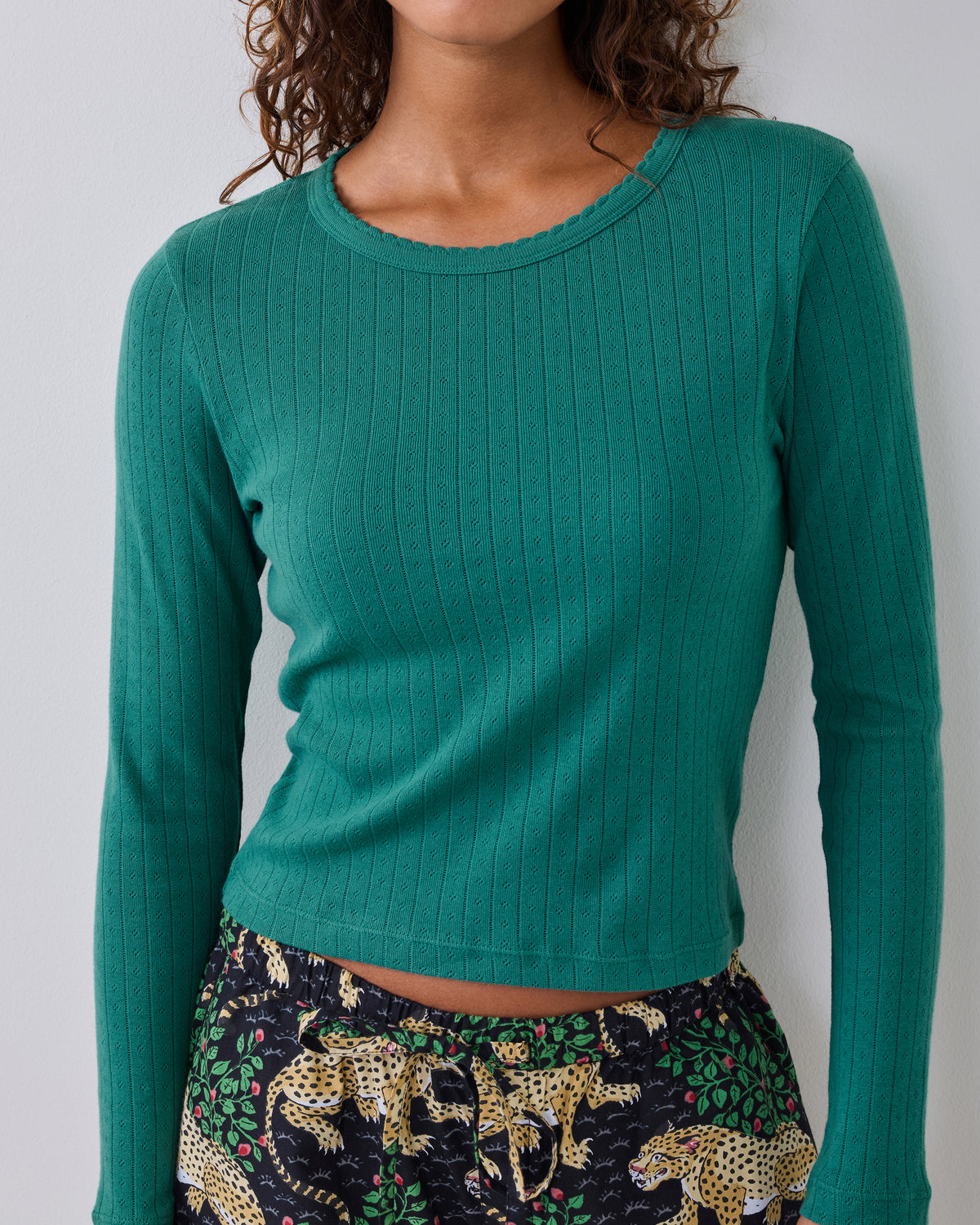 Cropped view of an evergreen long-sleeve pointelle shirt with a scalloped neckline, worn with printed pajama pants.
