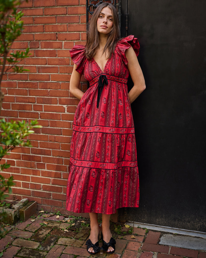 Front view of the Festive Roses Cecily Dress in Heirloom Red, showing its ruffled sleeves, waist tie, V-neckline, and tiered skirt outdoors.