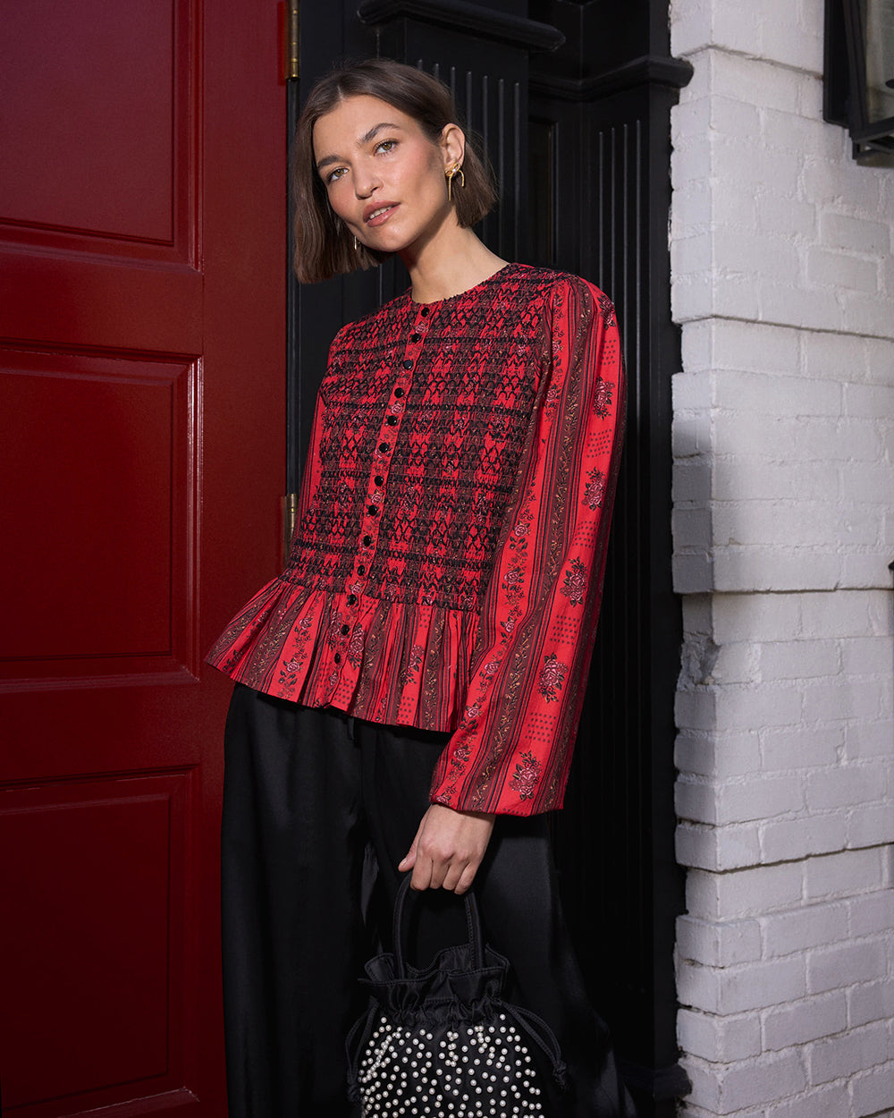 Person wearing a red long-sleeved blouse with a black patterned design and peplum hem.