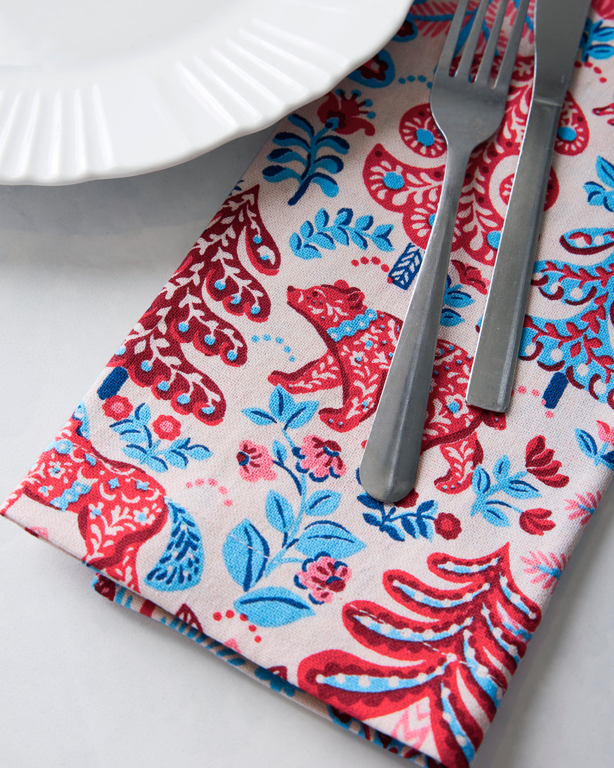 Close-up of a printed dinner napkin beneath a white plate and metal fork and knife.