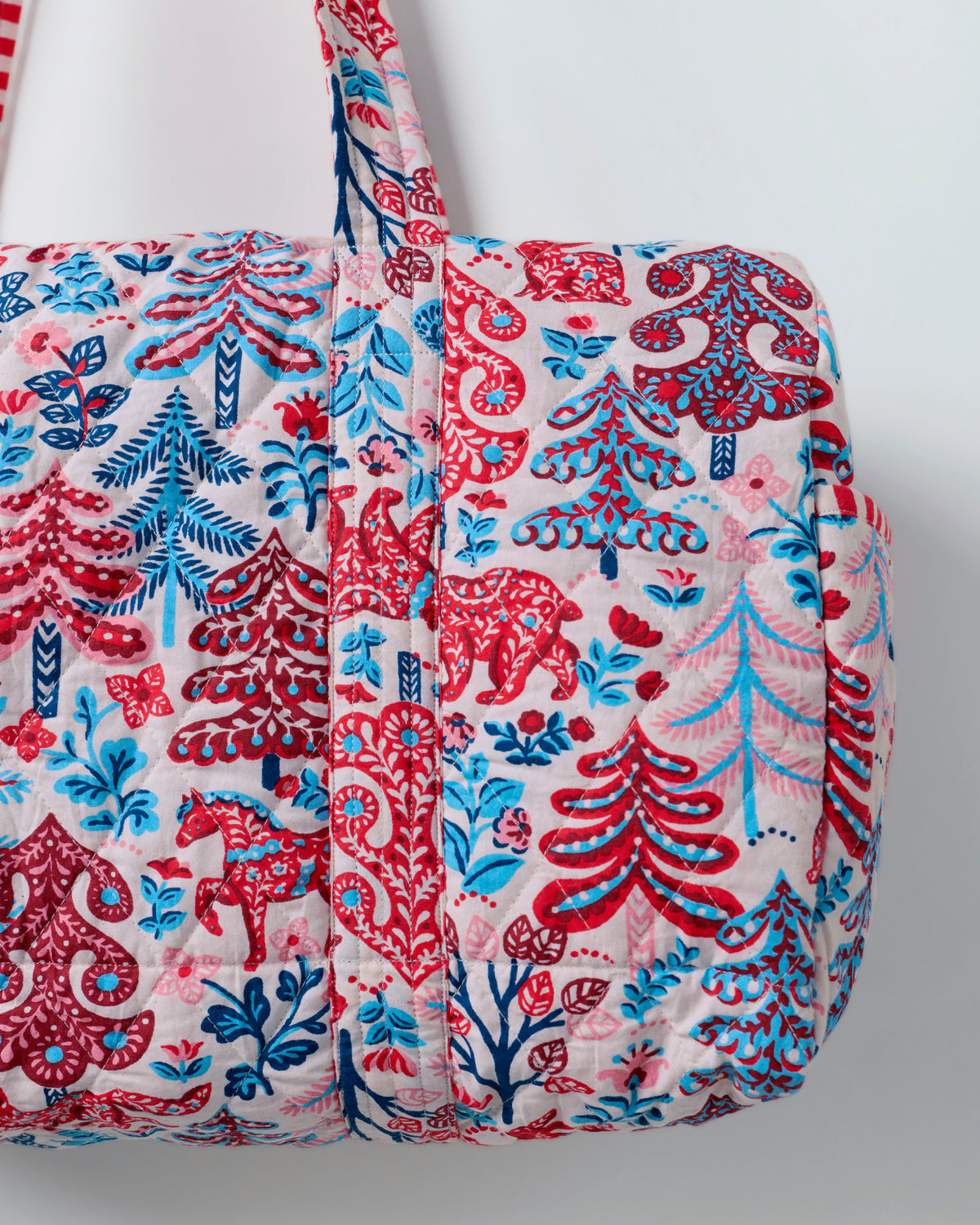 Close-up of the cream quilted duffle bag showing its patterned fabric, stitching, handle, and rounded end.