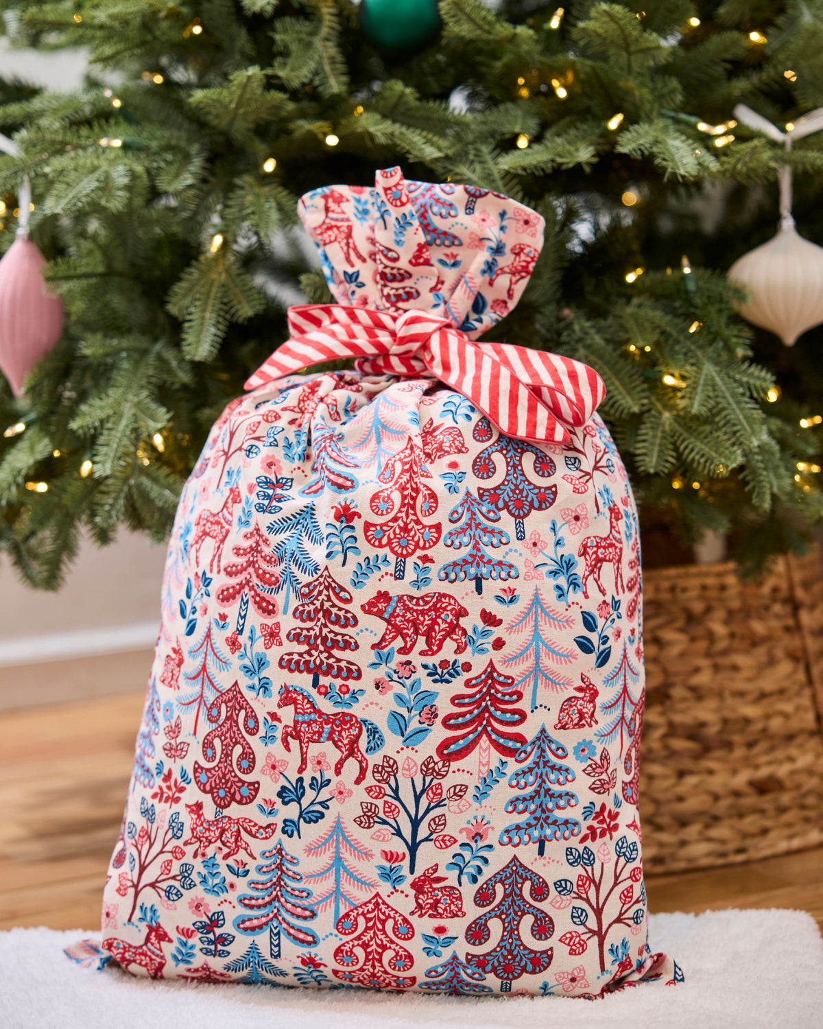 Folklore Forest gift sack tied with a red-and-white striped bow in front of a decorated Christmas tree.