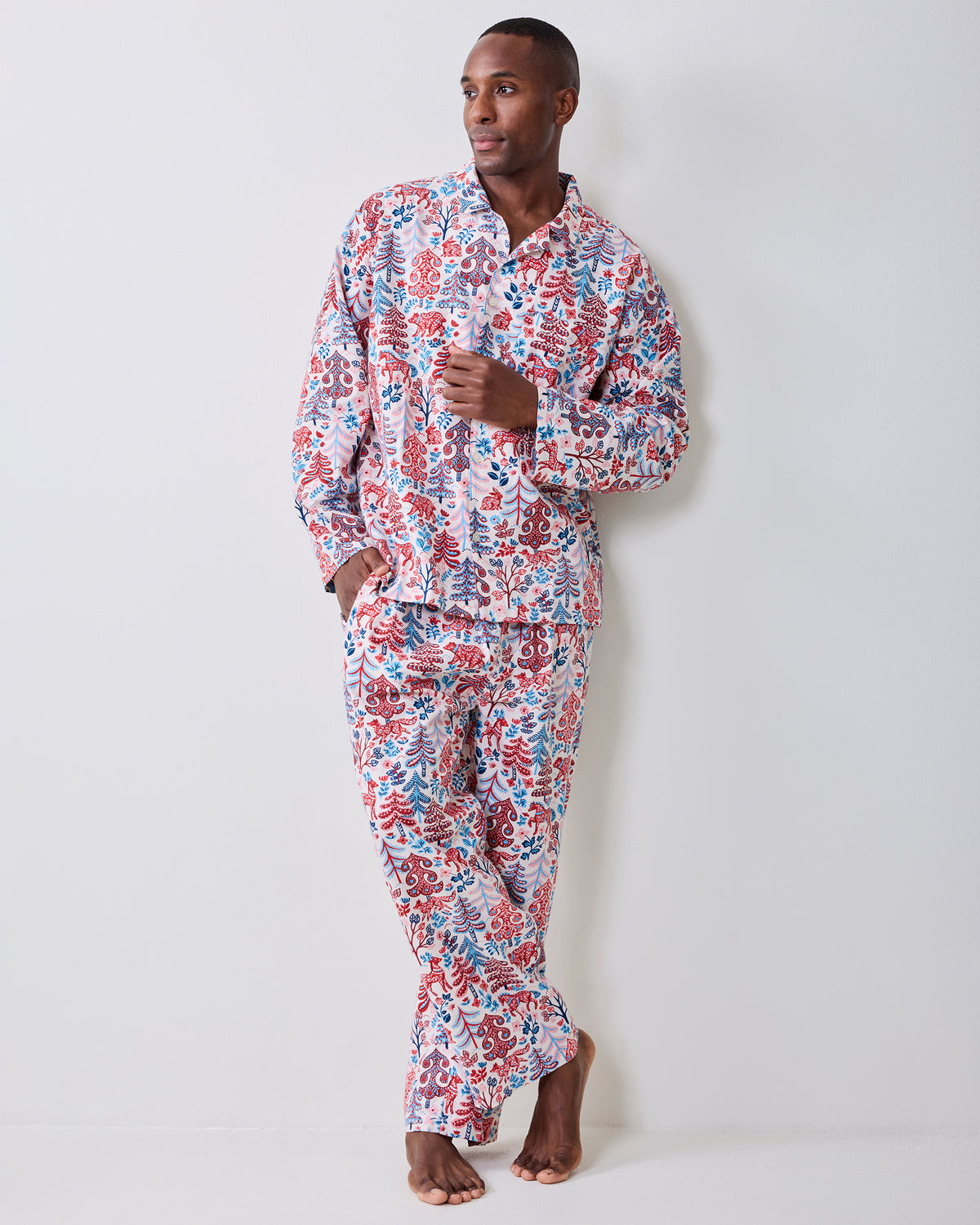 Full-length view of a person wearing the cream Folklore Forest men's long pajama shirt and pants with a red and blue forest print.
