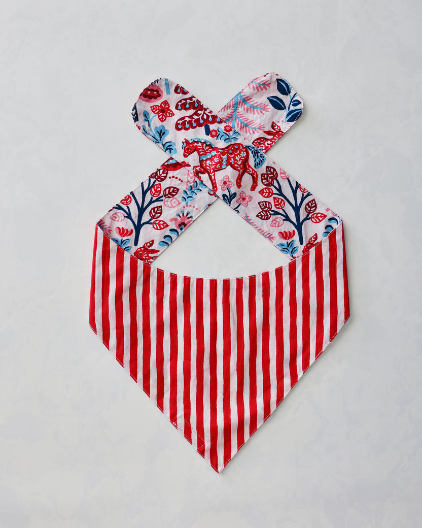 Reverse side of a pet bandana laid flat with red-and-white stripes and forest-patterned ties.