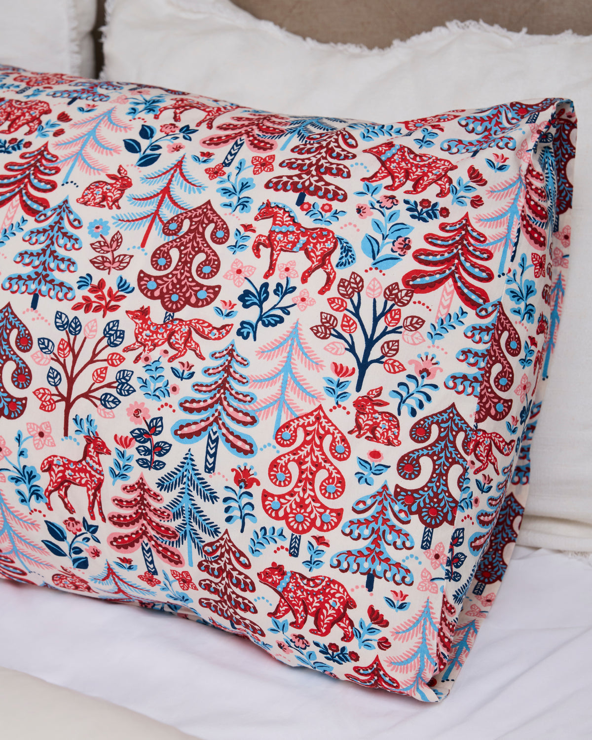 Close-up of a patterned pillowcase with red, navy, and pink forest motifs on a bed.