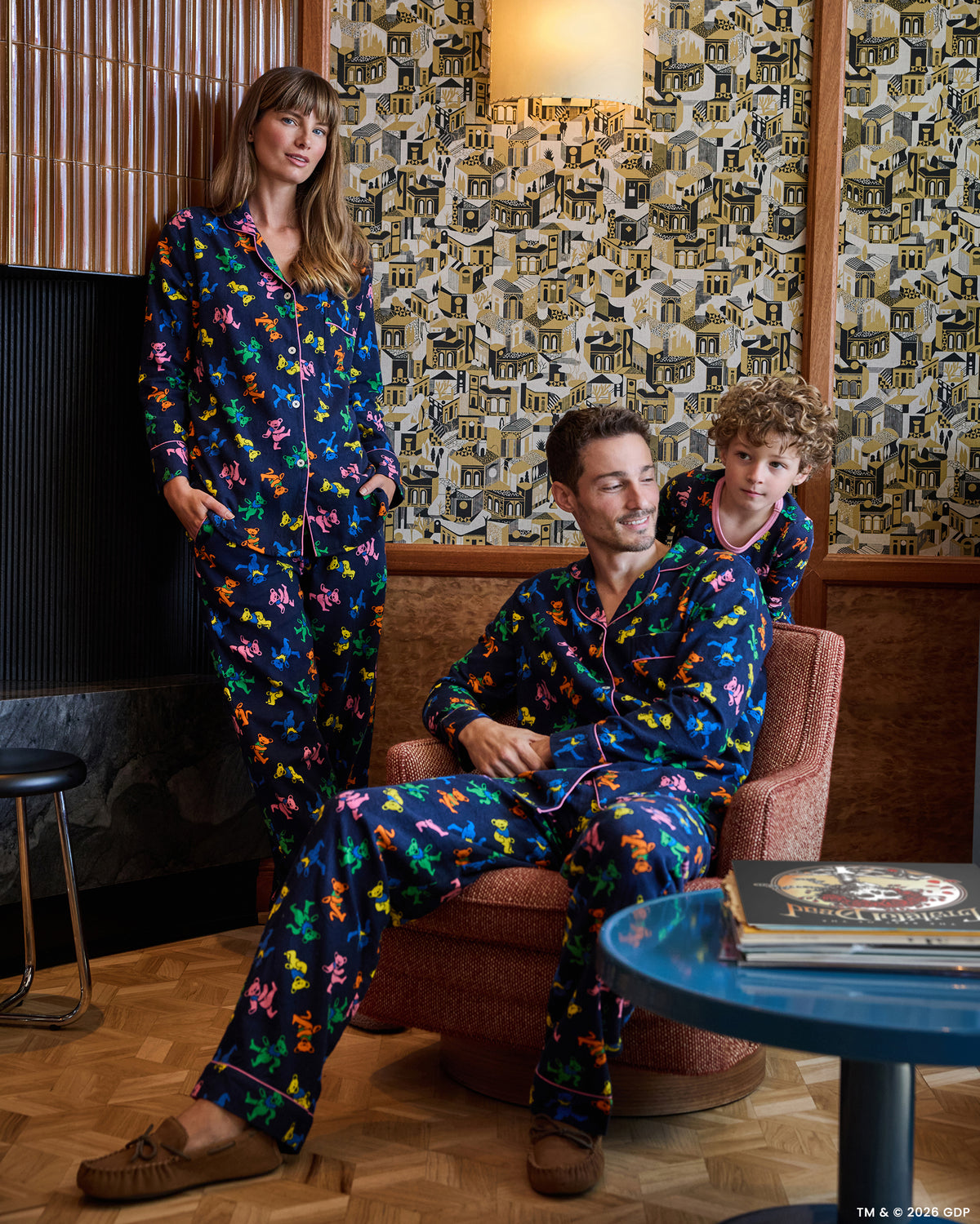 Three people wearing matching Dancing Bears long pajama sets in a furnished room.