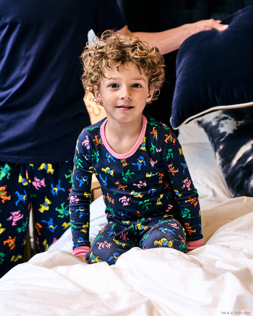 Child wearing the Dancing Bears kids snug fit long pajama set in Backstage Blue while sitting on a bed.