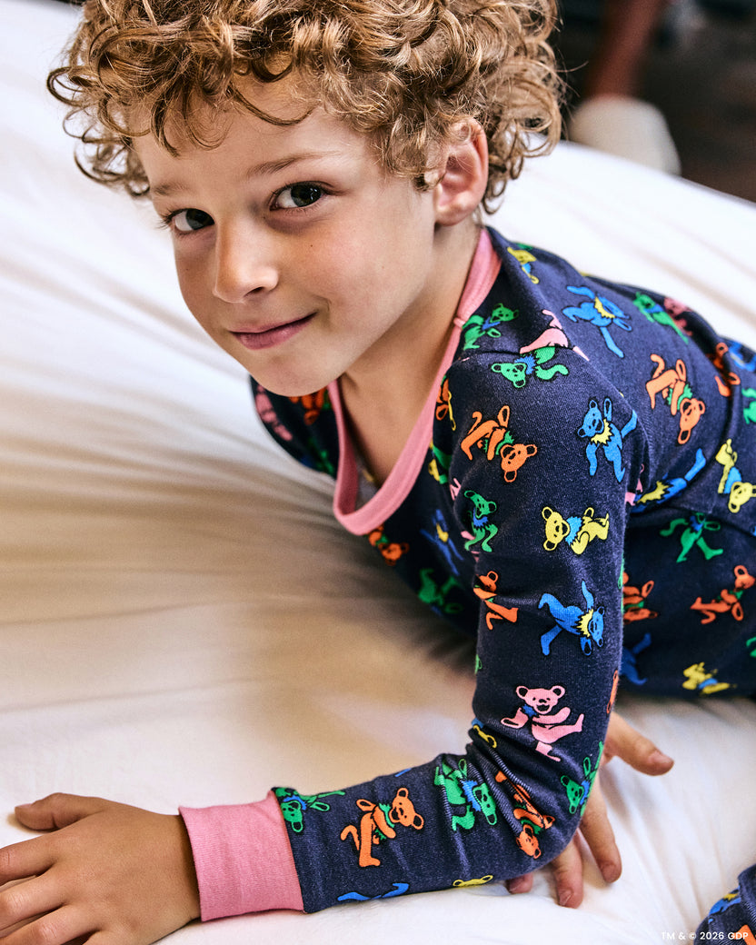 Close-up of a child wearing the Dancing Bears kids snug fit long pajama set in Backstage Blue while lying on a bed.