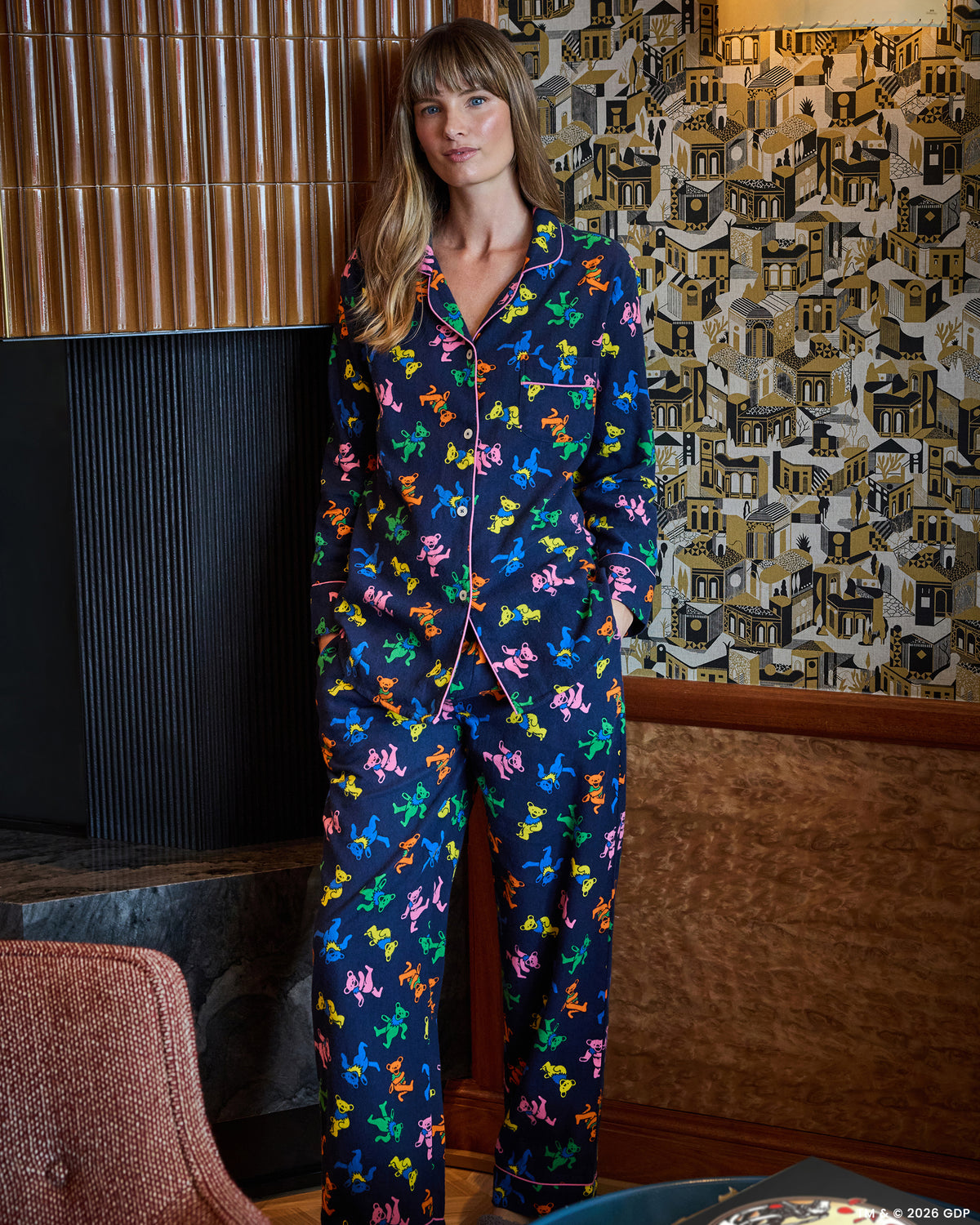 Full-body view of a person wearing a navy long pajama set with a multicolor dancing-bear print, button-front top, and long pants.