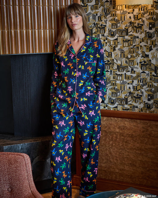 Full-body view of a person wearing a navy long pajama set with a multicolor dancing-bear print, button-front top, and long pants.