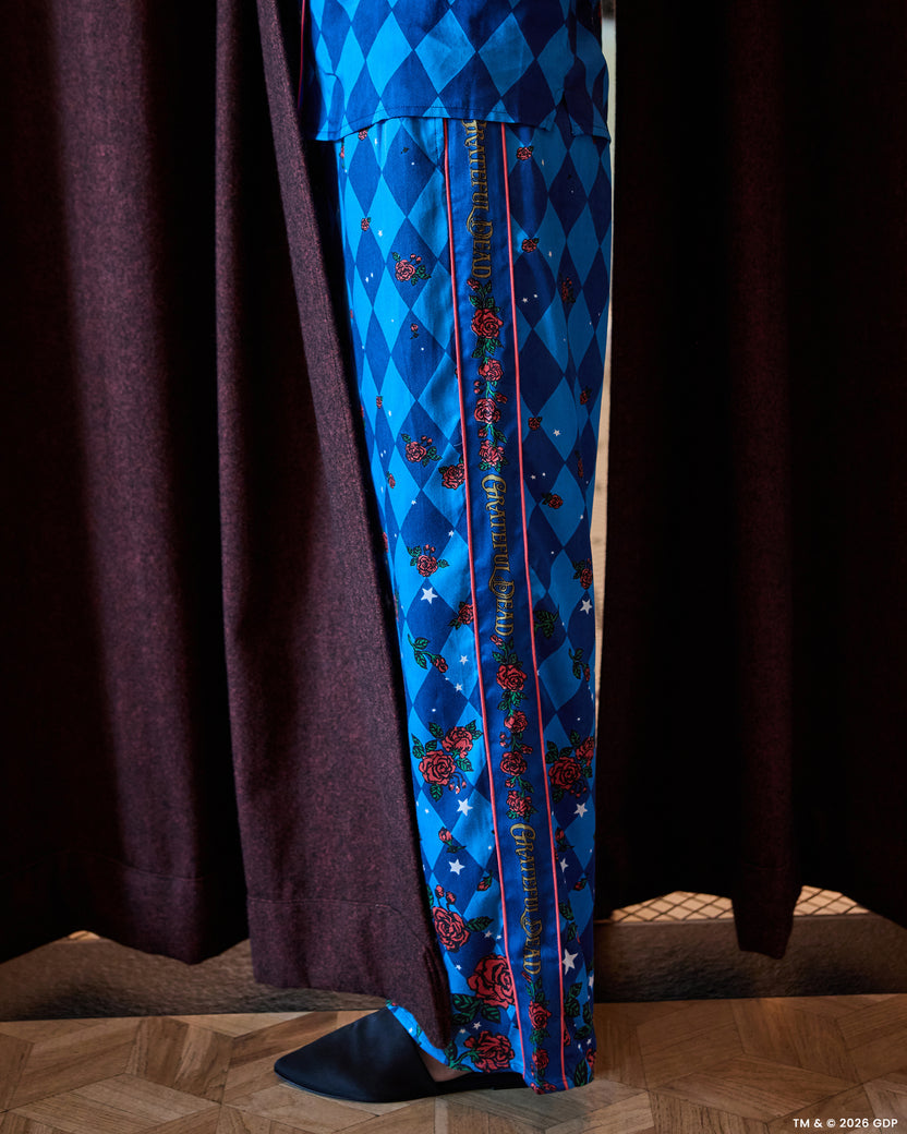Close view of blue diamond-patterned pajama pants with rose motifs, white stars, pink piping, and vertical decorative lettering.