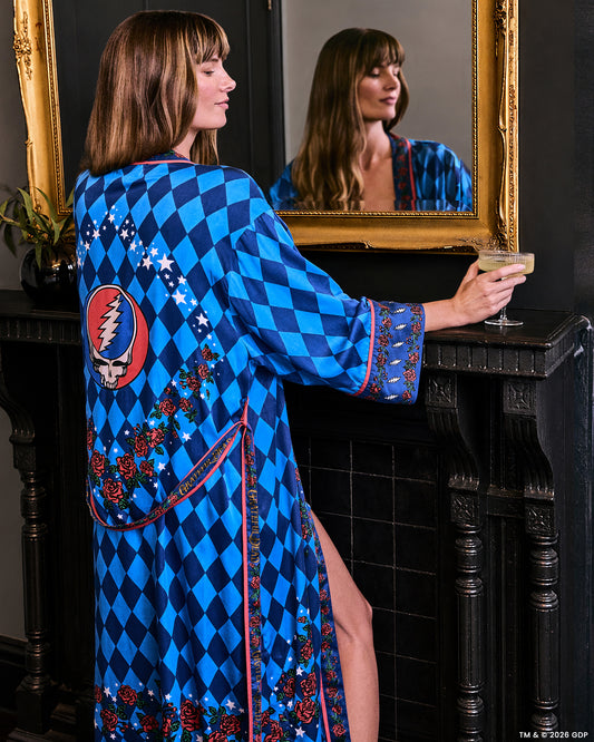 Back view of the blue argyle-print robe with rose and star trim and a large red oval skull-and-lightning graphic, shown in a mirror while holding a drink.