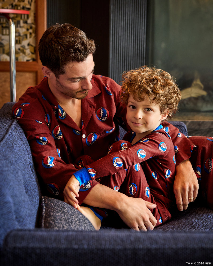 Adult and child seated together wearing matching red long-sleeved pajama sets with circular lightning-bolt motifs.