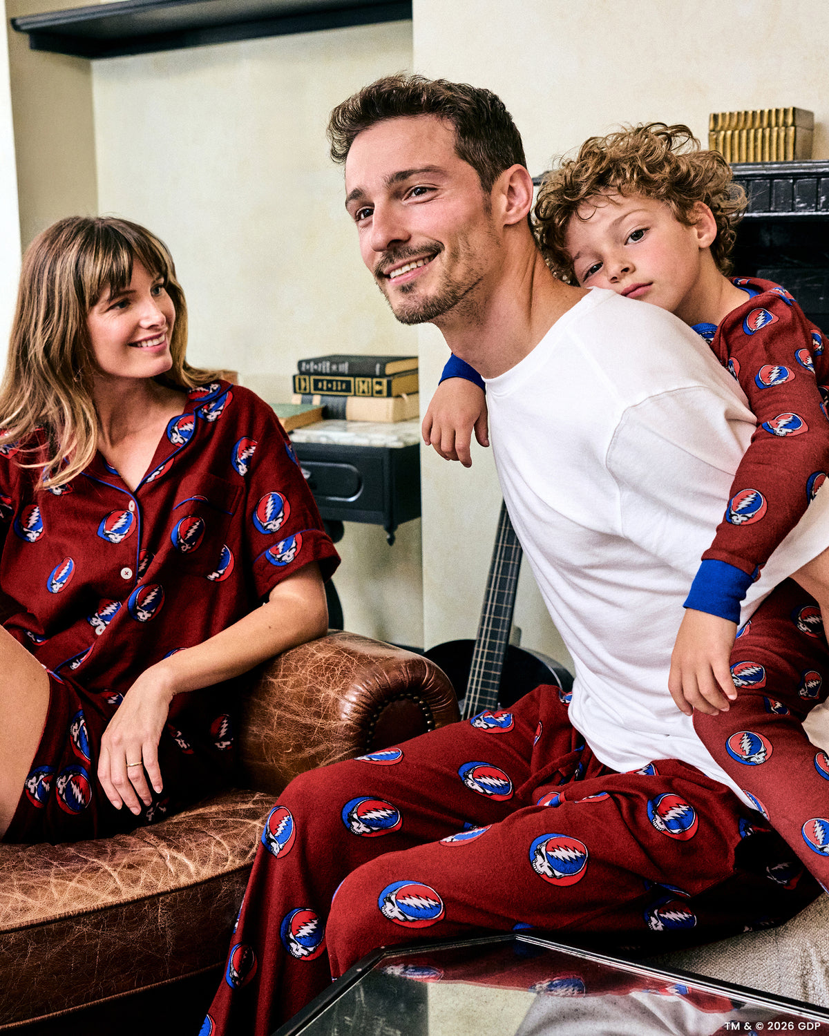 Child wearing a red printed pajama set while being held by an adult in a home interior.