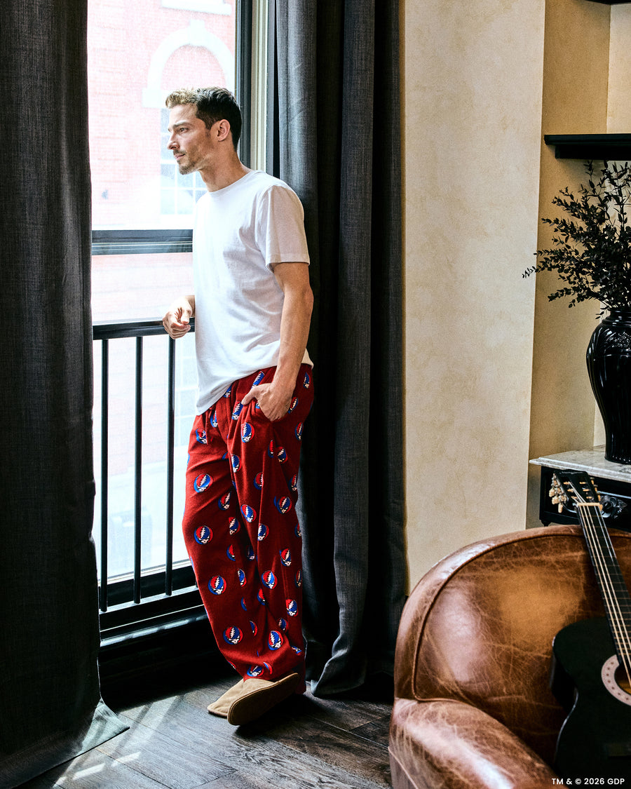 Person wearing red printed pajama pants and a white shirt beside a window.