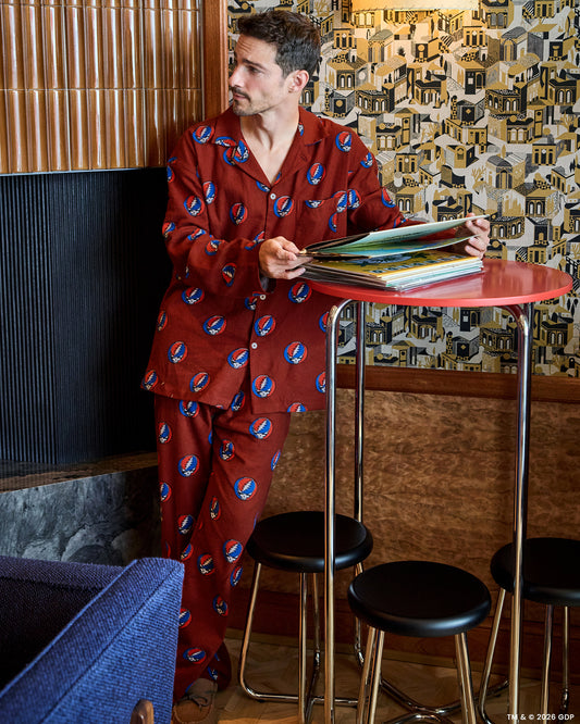 Person wearing a red long-sleeved pajama set with a repeating skull-and-lightning-bolt print while seated at a table.