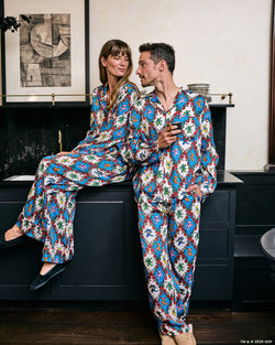 Two people wearing coordinated white pajama sets printed with colorful figures and red roses in an indoor setting.