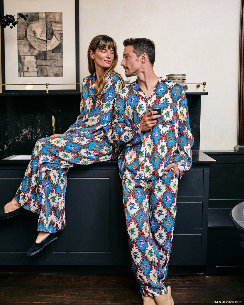 Two people wearing coordinated white pajama sets printed with colorful figures and red roses in an indoor setting.