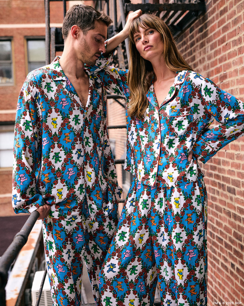 Two people wearing coordinated white pajama sets with colorful figures and red roses beside a brick wall.
